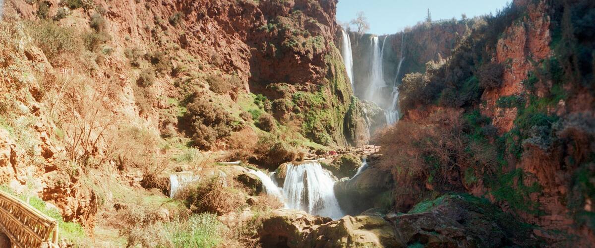 A canyon with a waterfall and a wooden bridge.