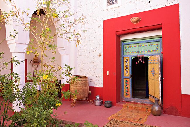 A red-walled building with a blue door, a large pot, and a small tree.
