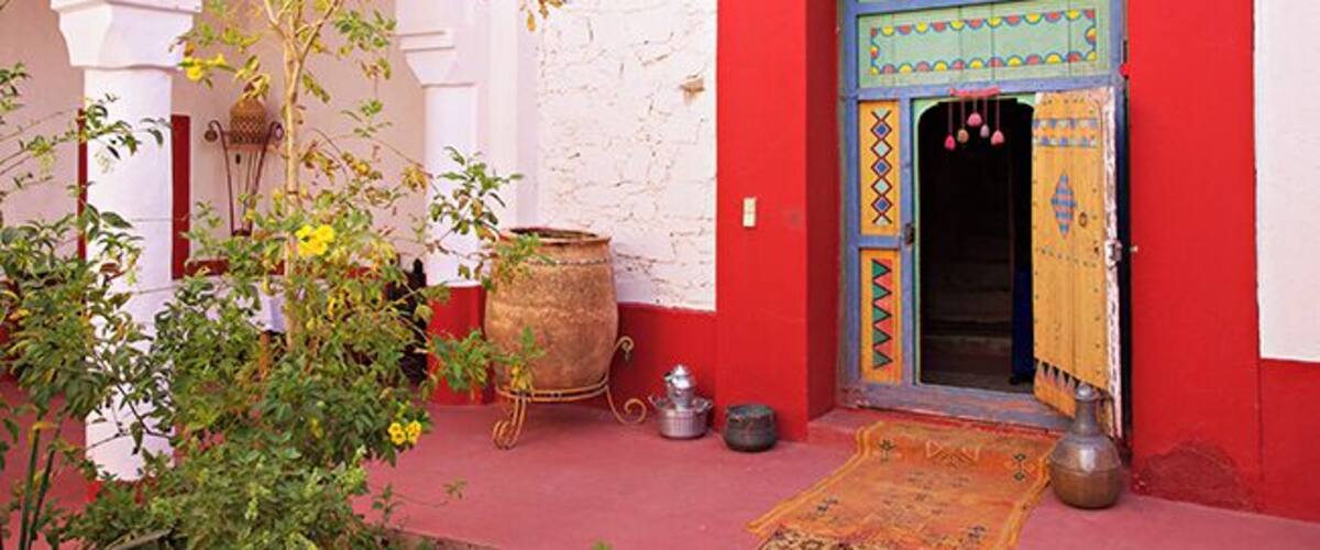 A red-walled building with a blue door, a large pot, and a small tree.