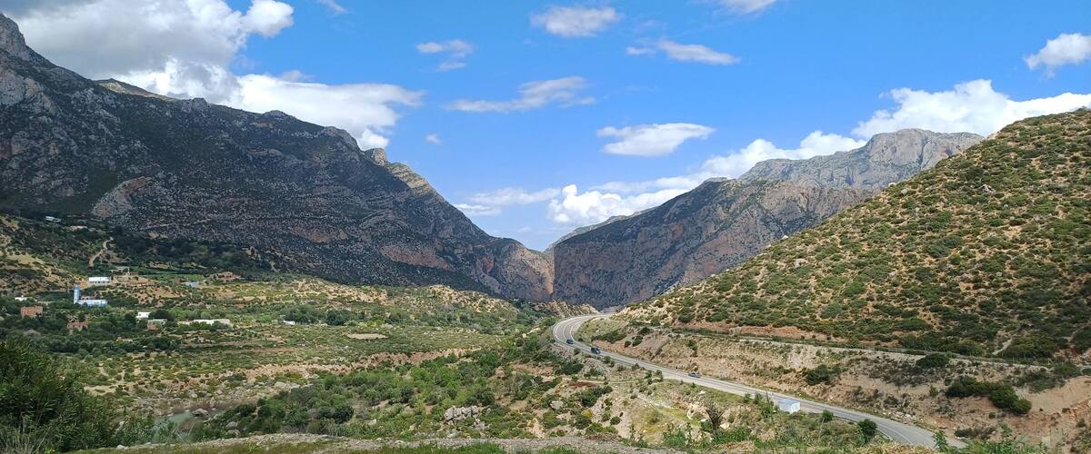 A winding mountain road through a valley with rocky mountains and sparse vegetation.