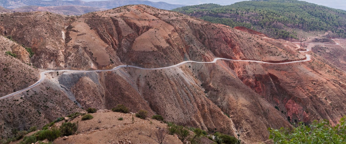 A winding road through a rugged, rocky landscape with sparse vegetation and distant green hills.