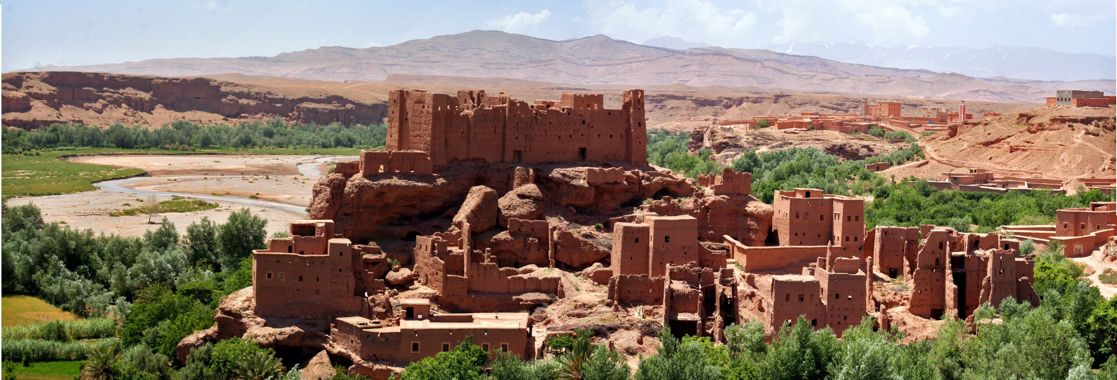 A desert landscape with ancient adobe structures and a river.