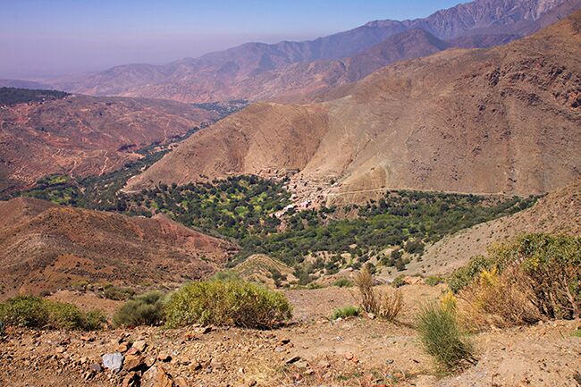 A mountainous landscape with a valley, rocky terrain, and sparse vegetation.
