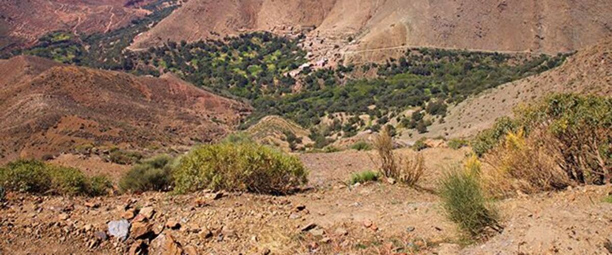 A mountainous landscape with a valley, rocky terrain, and sparse vegetation.