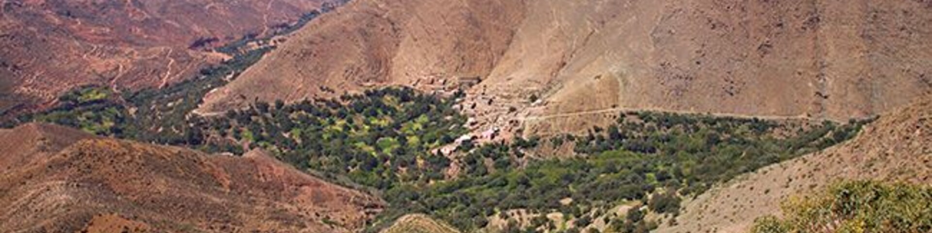 A mountainous landscape with a valley, rocky terrain, and sparse vegetation.