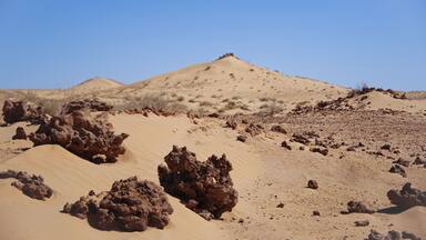 Dark rocks, a mountain and bright sand are forming a Lunar landscape in the Sahara Desert