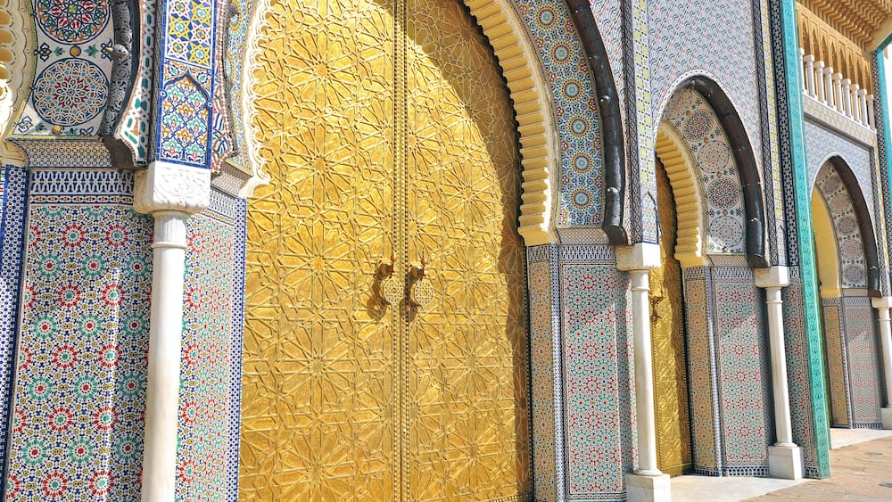 A large ornate door with intricate tile patterns and a golden finish, flanked by smaller arched windows with detailed designs.