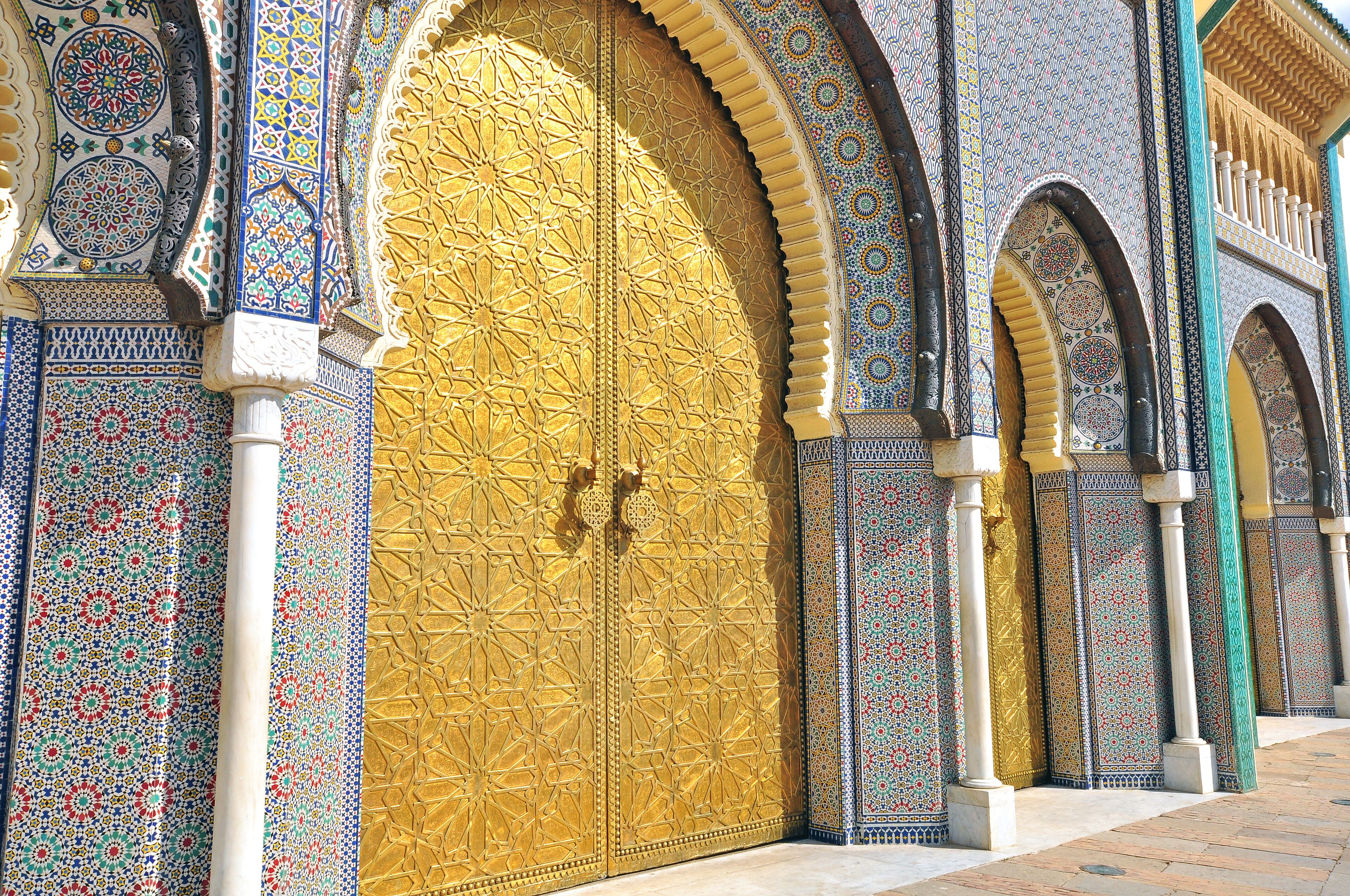 A large ornate door with intricate tile patterns and a golden finish, flanked by smaller arched windows with detailed designs.