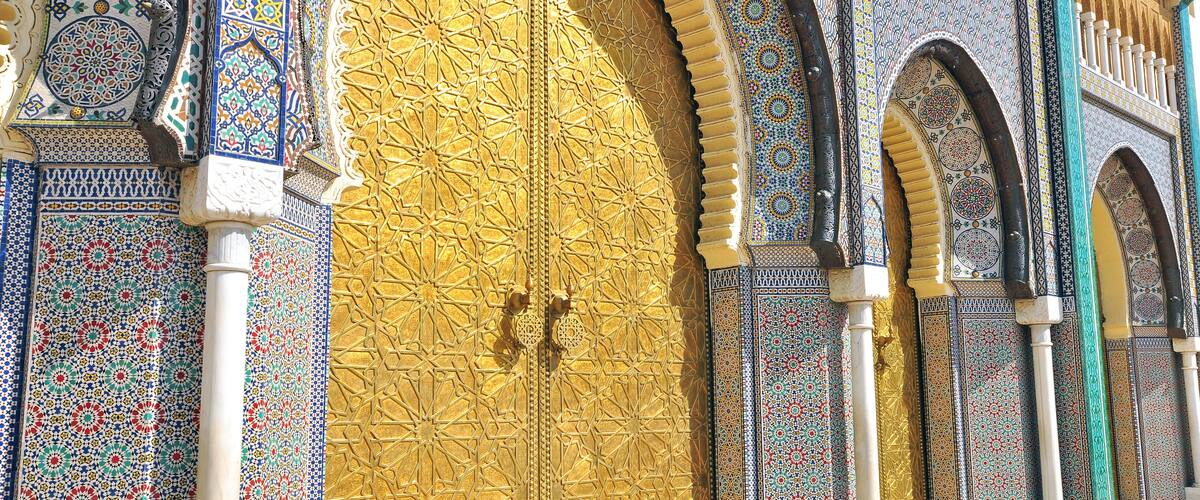 A large ornate door with intricate tile patterns and a golden finish, flanked by smaller arched windows with detailed designs.