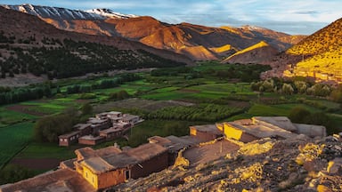 Un paisaje montañoso con campos en terrazas, un pueblo con edificios tradicionales y picos nevados a lo lejos.