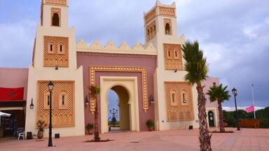 A traditional Moroccan gate with intricate designs, palm trees, and a clear sky.