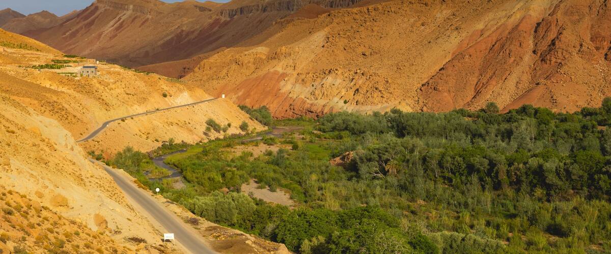 A winding road through a mountainous landscape with sparse vegetation and a small building on the left.