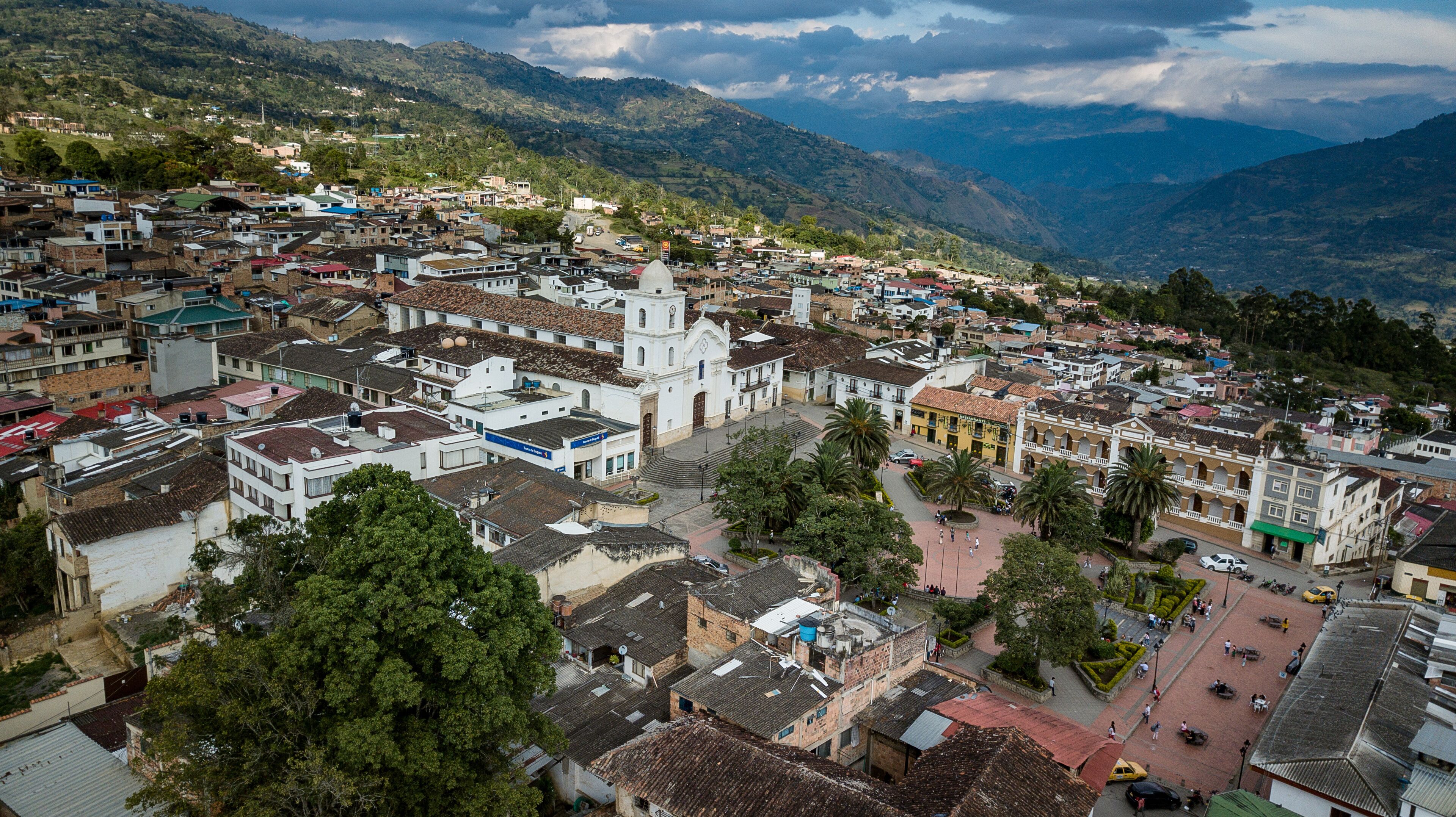 A town with a prominent church, surrounded by mountains and greenery.