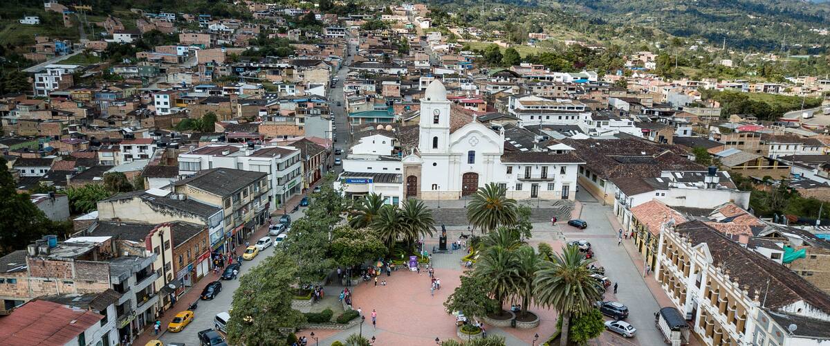 A town with a prominent white church, a central plaza with palm trees, and a dense residential area.