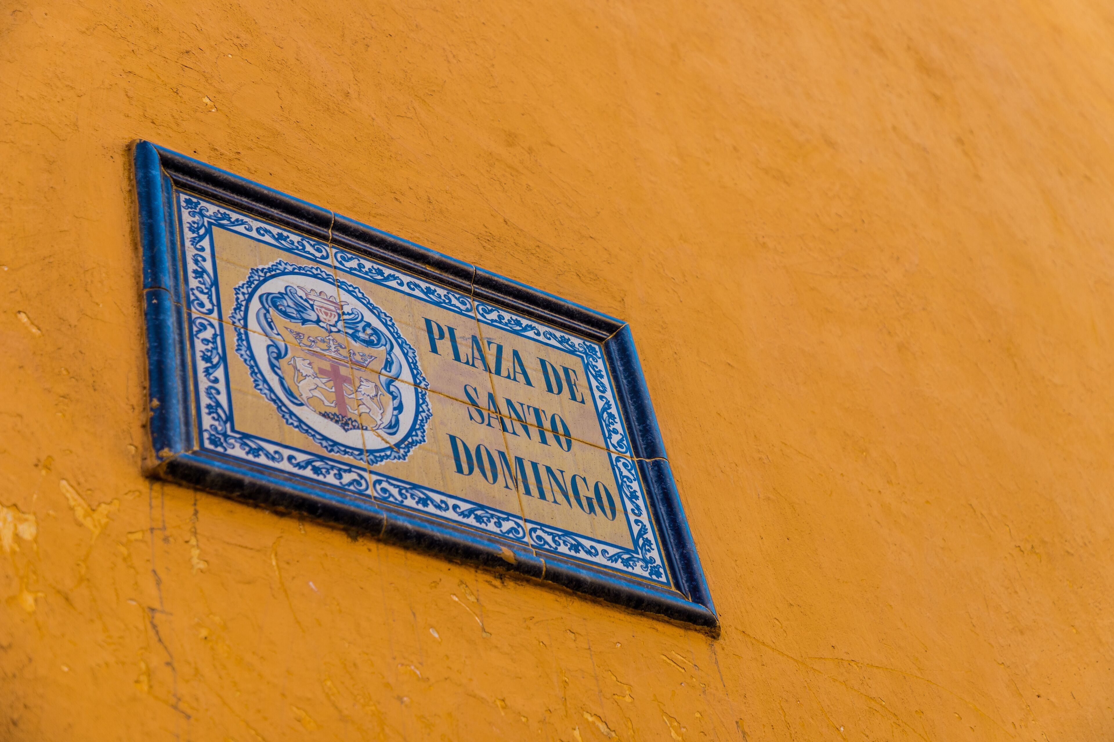 A sign with the text "PLAZA DE SANTO DOMINGO" on a yellow wall.