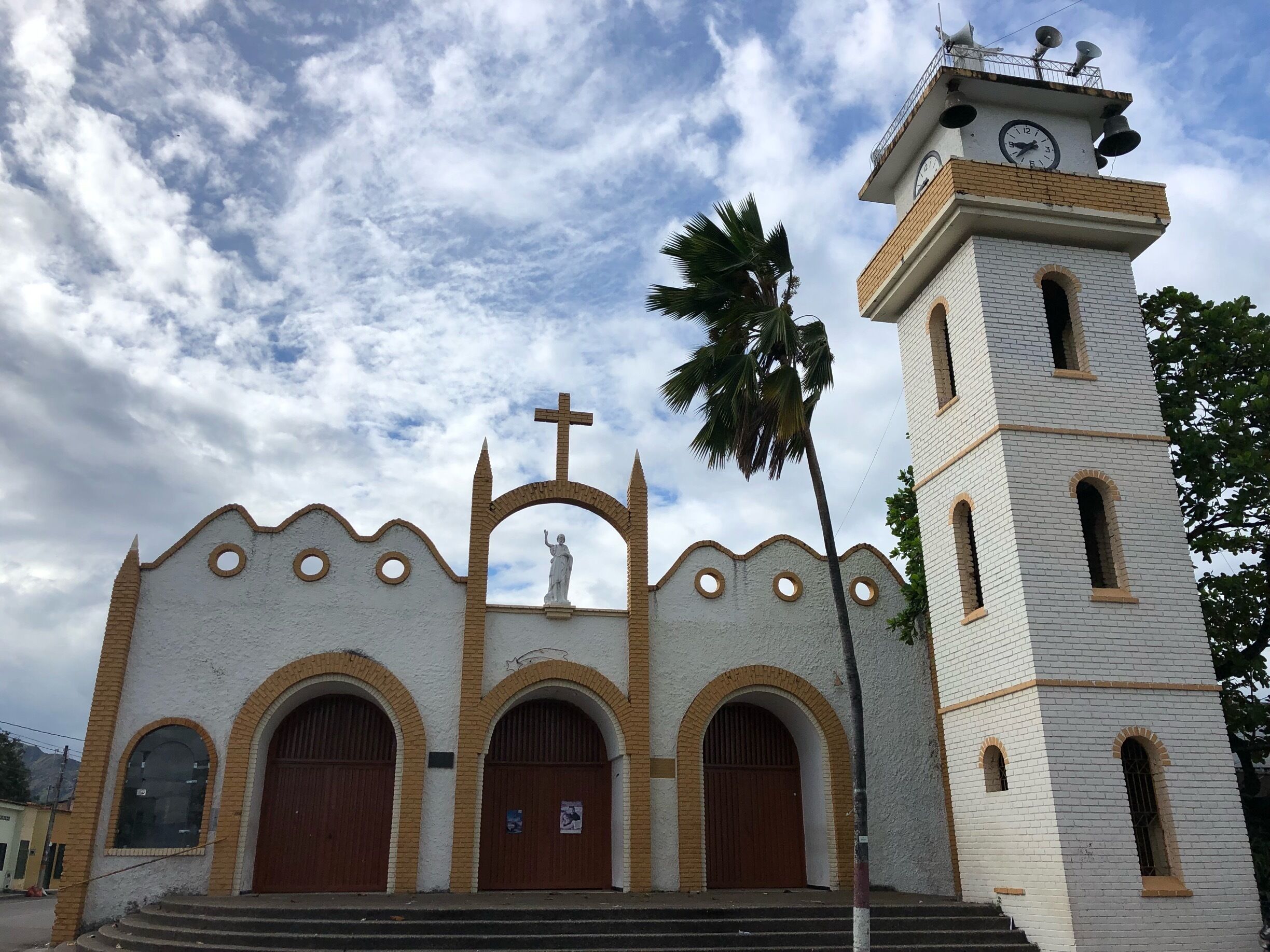 A church with a bell tower, arched doors, and a cross on top.