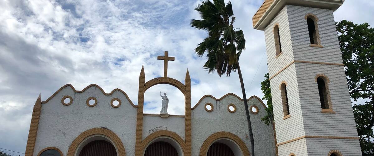 A church with a bell tower, arched doors, and a cross on top.