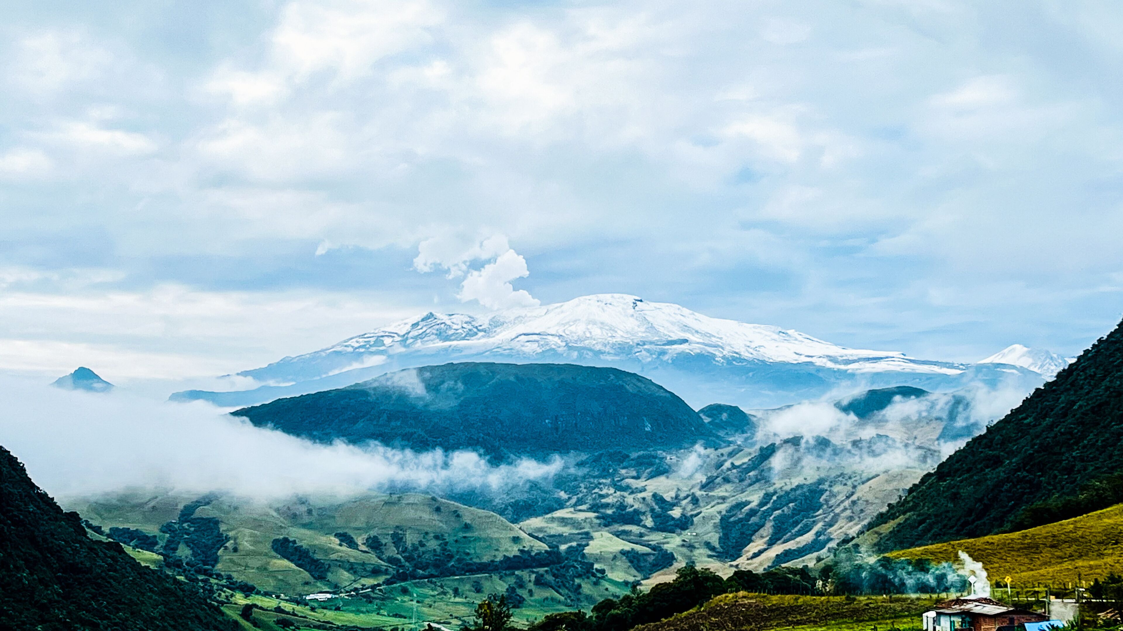 A snow-capped mountain, lush green valleys, and a small building in the foreground.
