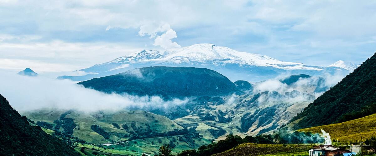 A snow-capped mountain, lush green valleys, and a small building in the foreground.