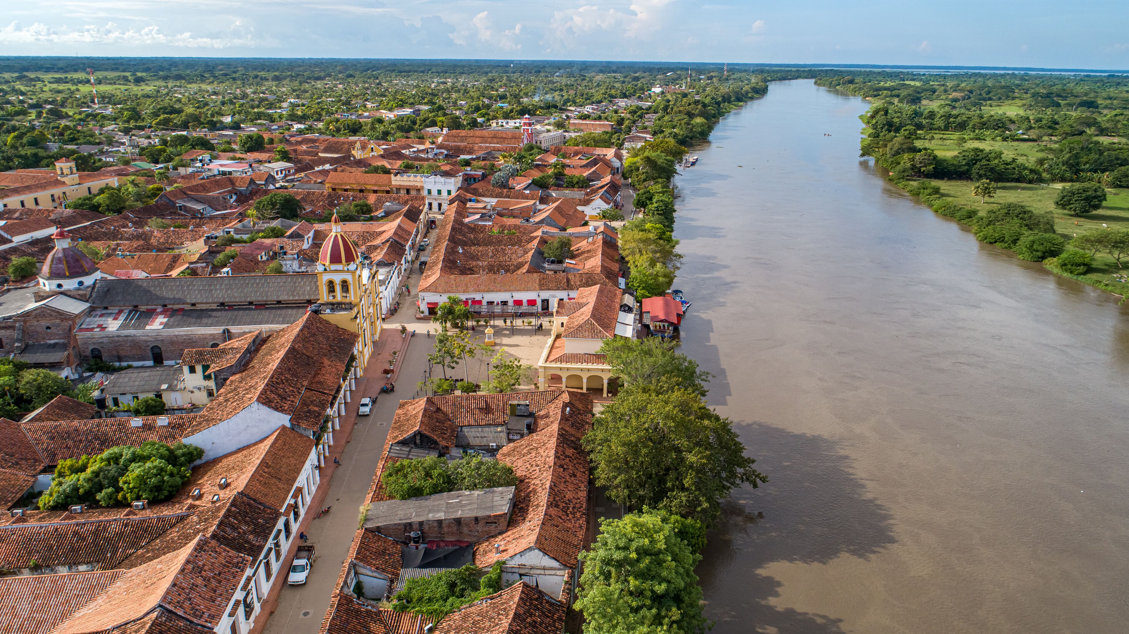 A river flowing through a town with red-tiled roofs and a prominent church with a dome.