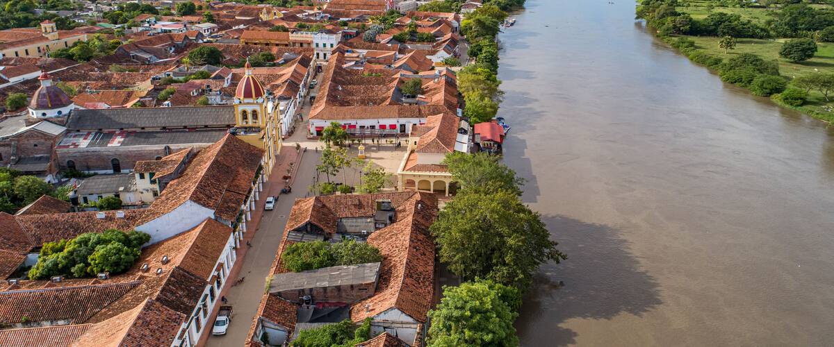 A river flowing through a town with red-tiled roofs and a prominent church with a dome.