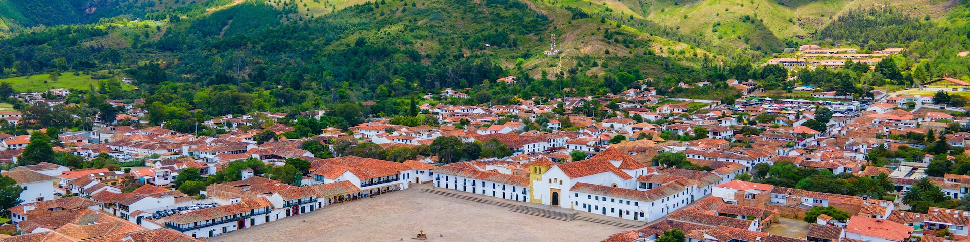 A town with red-tiled roofs nestled in a valley surrounded by green hills.