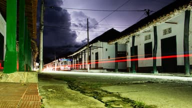 Rua à noite com um trem passando, edifícios com portas verdes e céu nublado.