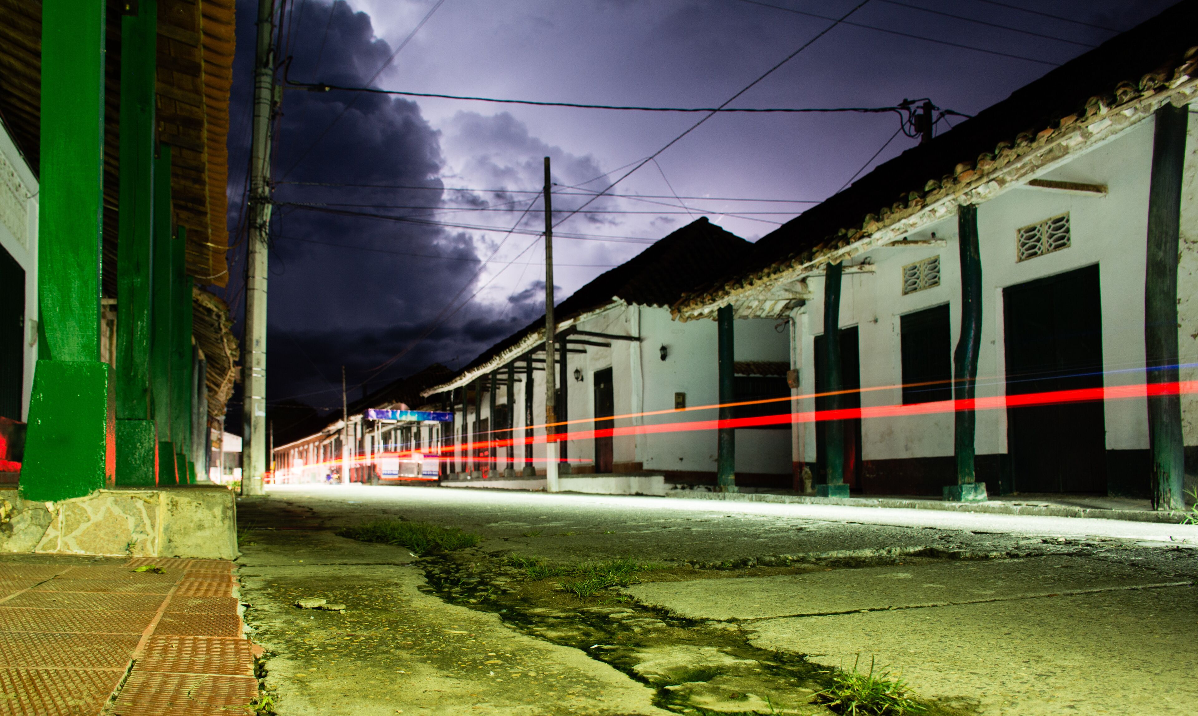 A street at night with a train passing by, buildings with green doors, and a cloudy sky.