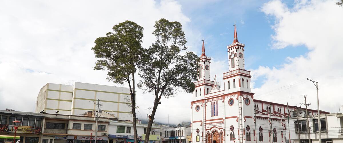 A plaza with a prominent church featuring a tall spire and clock tower, surrounded by trees and various buildings.