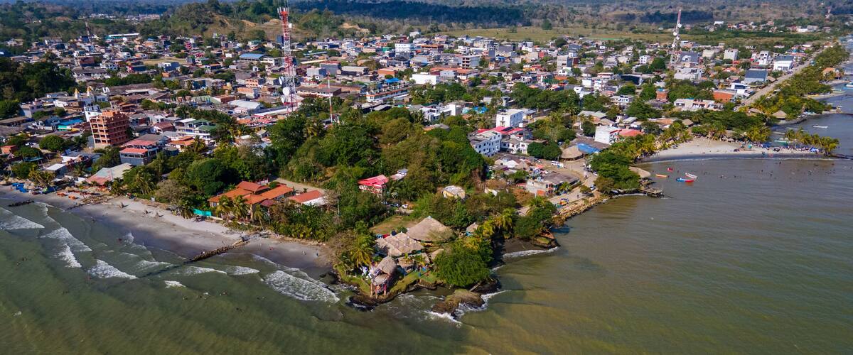 An aerial view of a coastal town with a beach, houses, and a lighthouse.
