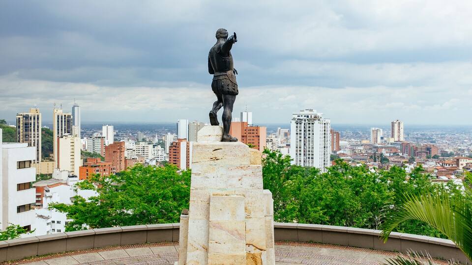 A statue of a man pointing upwards, surrounded by a circular plaza, with a cityscape in the background.