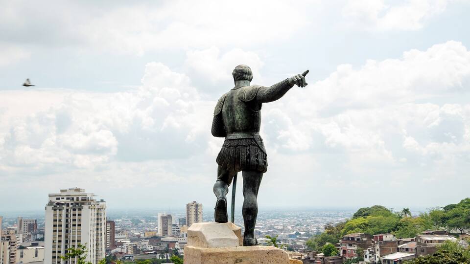 A statue of a man pointing to the cityscape in the background.