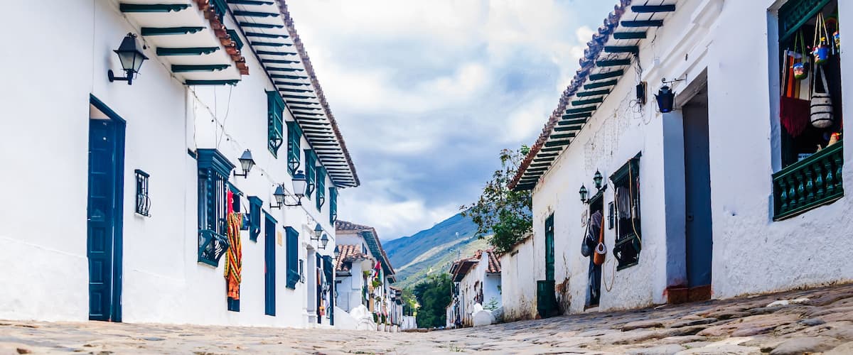 A cobblestone street lined with white buildings with green shutters and blue doors.