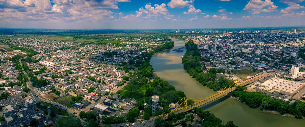 An aerial view of a city with a river running through it, a bridge, and surrounding greenery.