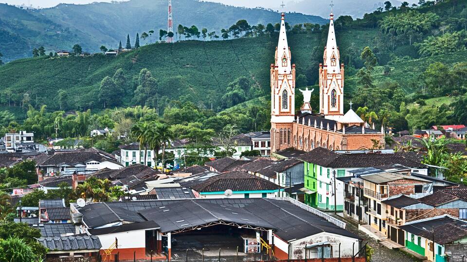 A church with two tall spires, surrounded by a hillside village with houses.