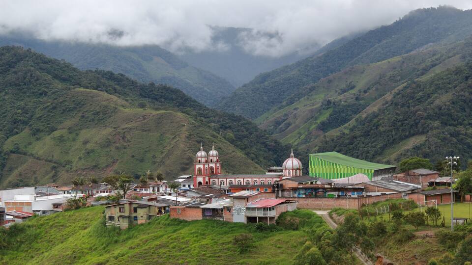 A valley with a church, a sports field, and lush green hills.