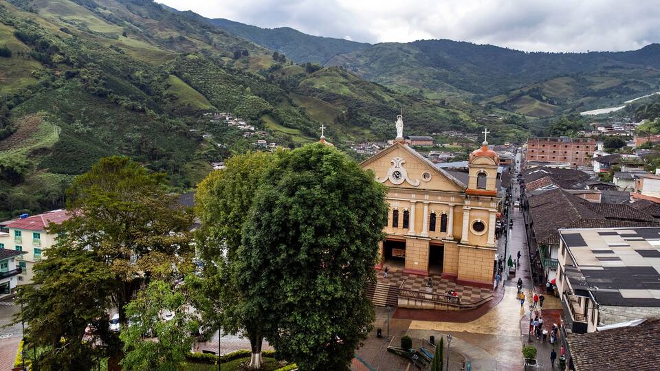 A town with a prominent church, lush green hills, and a large tree in the foreground.