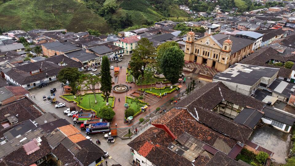 A town with a central plaza, historic buildings, and terraced fields in the background.