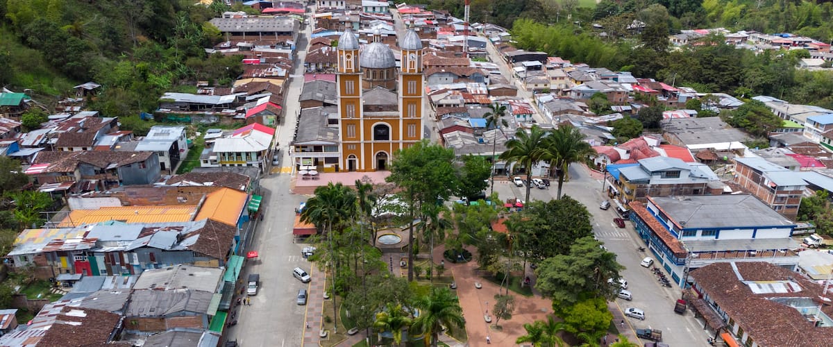 A town with a prominent church featuring two domes, surrounded by colorful buildings and palm trees.