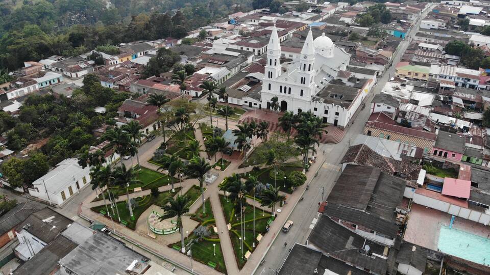 An aerial view of a town with a prominent white church with a dome and a tall bell tower, surrounded by residential buildings and palm trees.