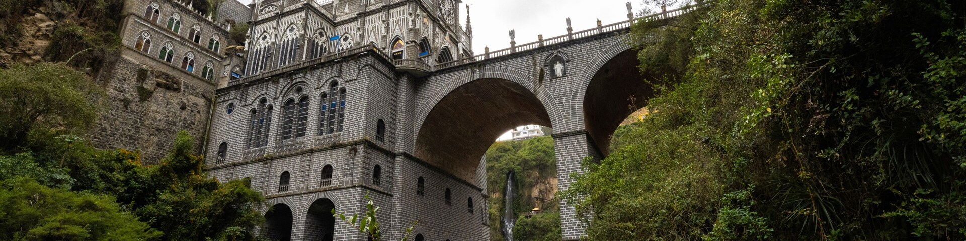 Un castillo de estilo gótico con un gran puente arqueado sobre un valle verde exuberante.