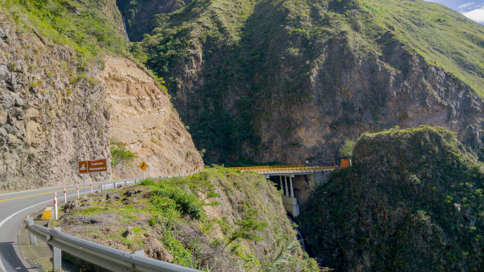 A road with a guardrail, a bridge, and a steep cliff.