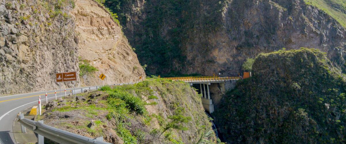 A road with a guardrail, a bridge, and a steep cliff.