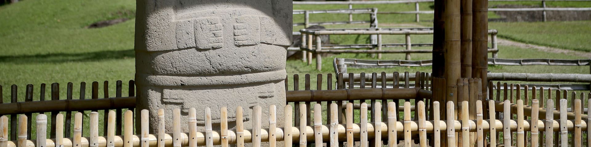 A stone statue with a carved face, a bamboo fence, and a pavilion in the background.