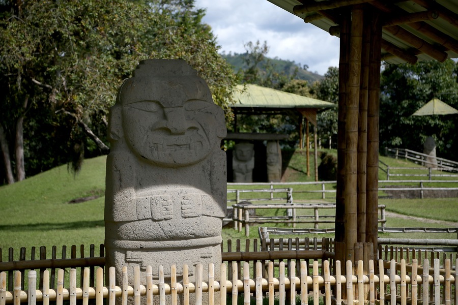 A stone statue with a carved face, a bamboo fence, and a pavilion in the background.