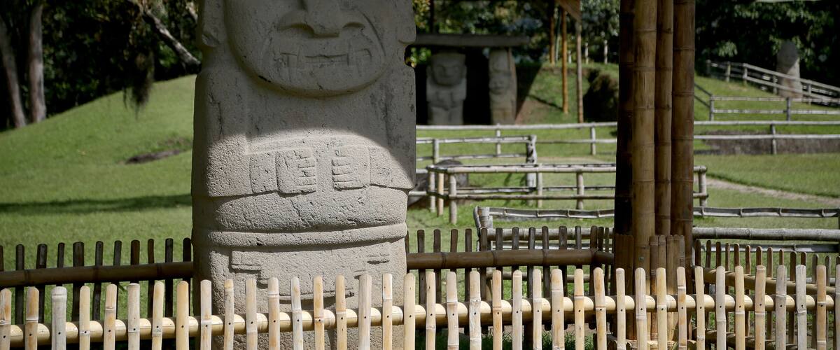 A stone statue with a carved face, a bamboo fence, and a pavilion in the background.