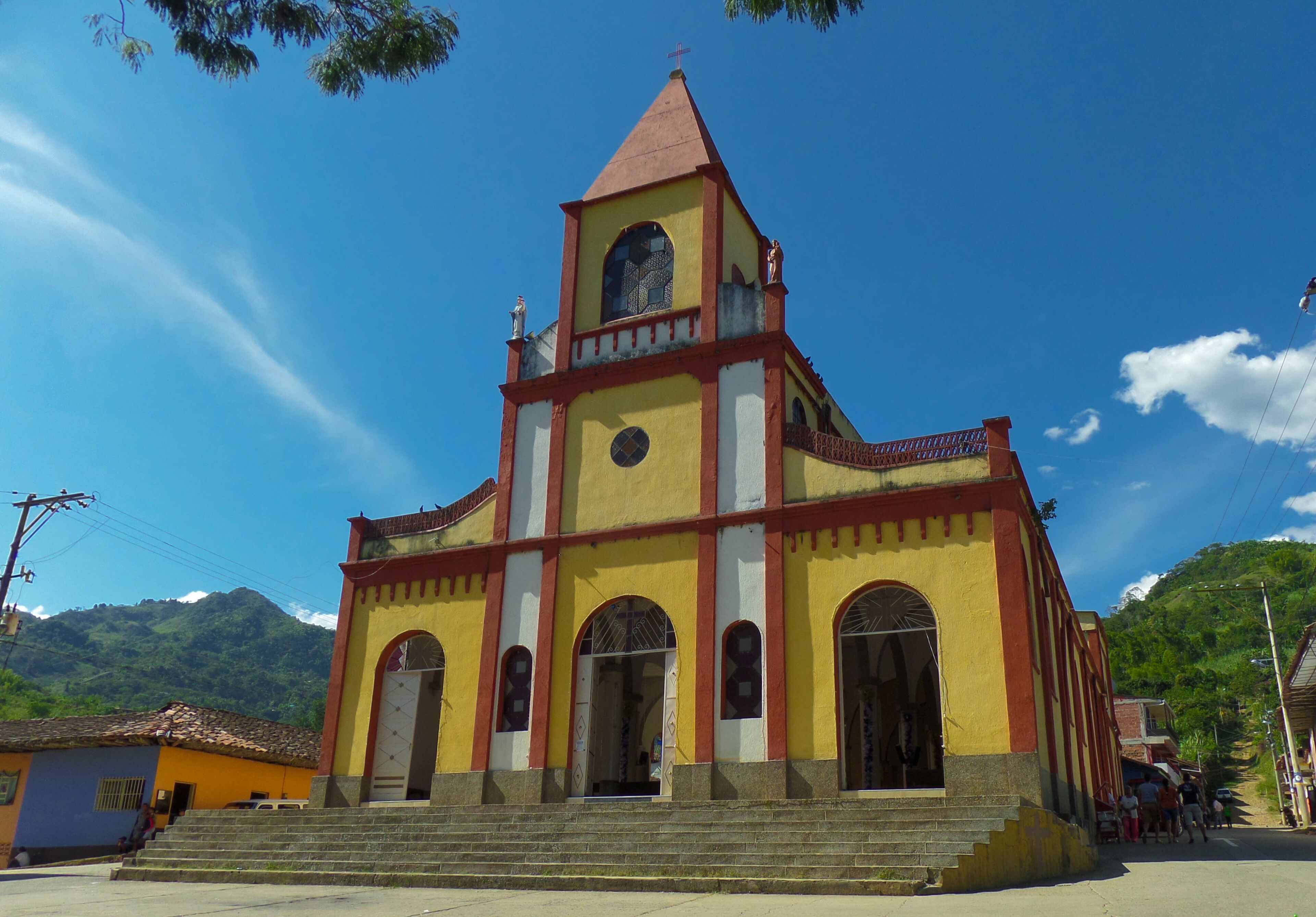 A church with a red roof and yellow walls, set against a mountainous backdrop.