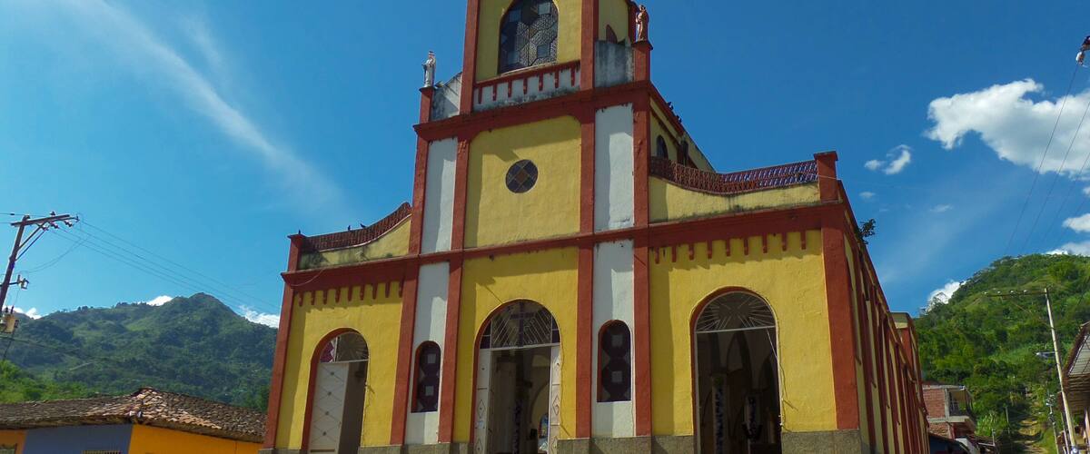 A church with a red roof and yellow walls, set against a mountainous backdrop.