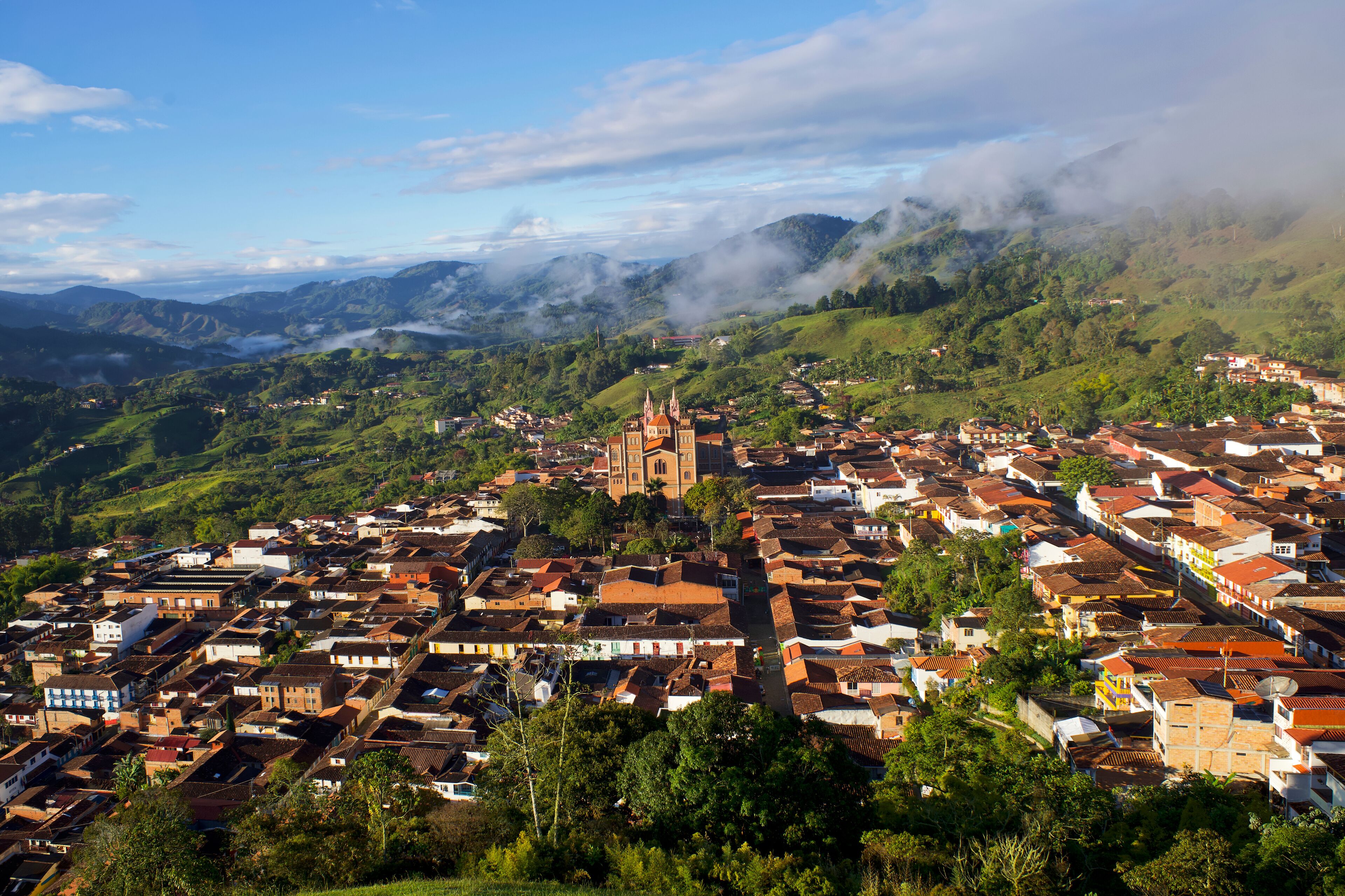 A town with a prominent church on a hill, surrounded by lush green hills and a clear sky.