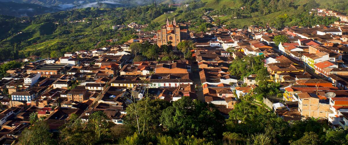 A town with a prominent church on a hill, surrounded by lush green hills and a clear sky.